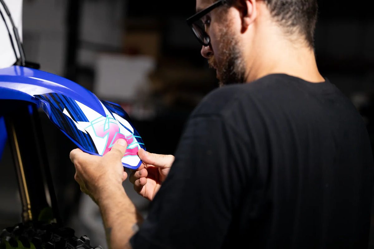 Team member working beside a blue motocross bike with custom graphics in the workshop.