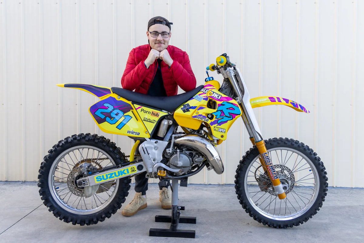 Rider standing behind a yellow Suzuki motocross bike with custom graphics