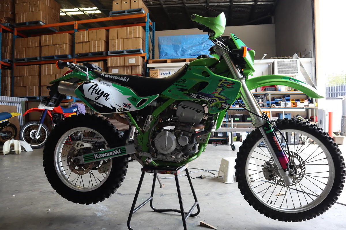 Green Kawasaki dirt bike with Aiya custom graphics in Omega's workshop.